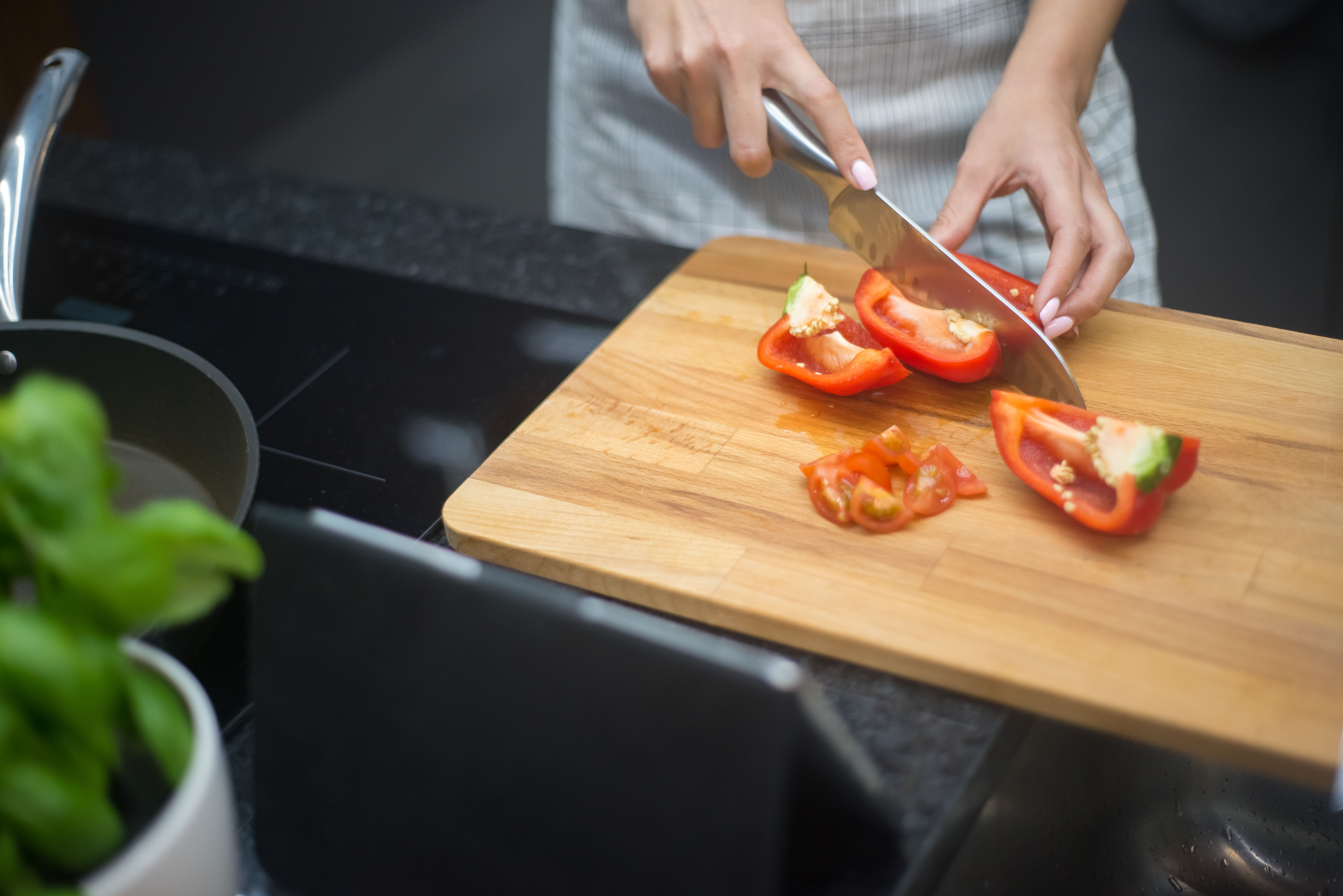 Close-up of a woman slicing red bell pepper in a modern kitchen.